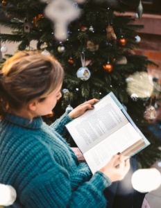 Photo of a woman reading a book by a christmas tree for a seasonal promotion