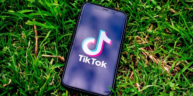 a mobile phone lying on green grass with the tiktok app open